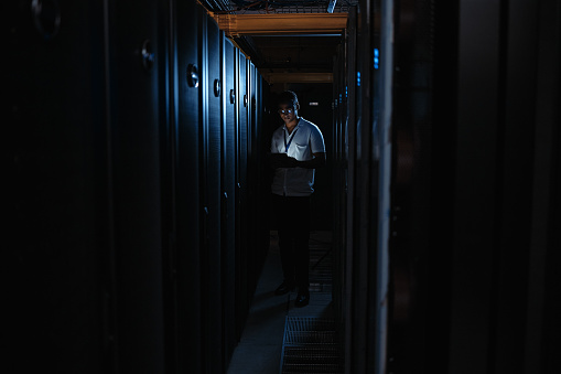 IT computer technician fixing a server mainframe in a dark data centre at night. Professional engineer, developer and programmer uploading software, repairing malware system and coding data interface