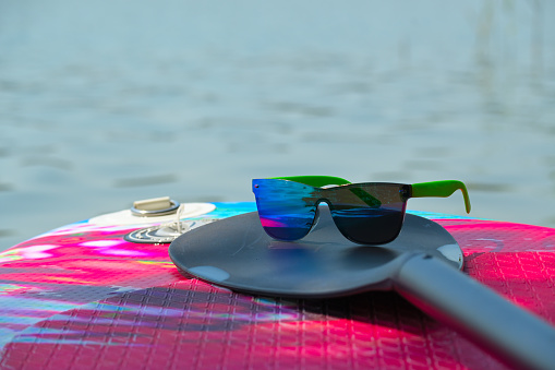 Paddle and sunglasses on SUP paddle-board in a tranquil lake with reflections on the water