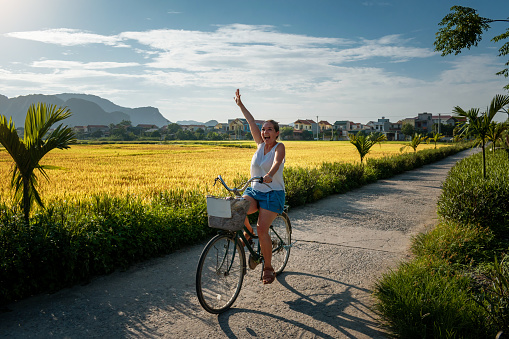 Woman tourist riding a bicycle through rice fields in Vietnam. Young woman riding a bike. Tourist on bicycle in Ninh Binh, Vietnam. Happy woman on her bike