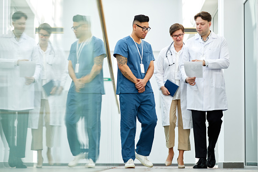 Full length portrait of doctors walking towards camera in hall of modern clinic and holding clipboards, copy space