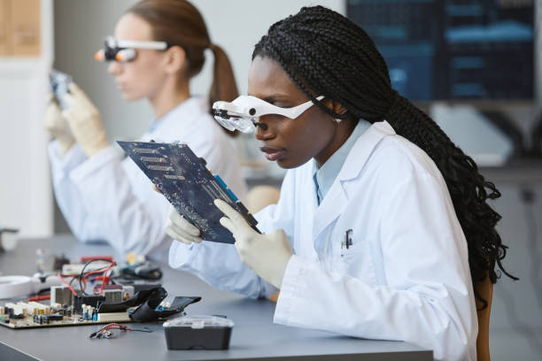 Engineers Working with Tech Portrait of young black woman wearing magnifying glasses and inspecting electronic parts in quality control lab african american scientist stock pictures, royalty-free photos & images