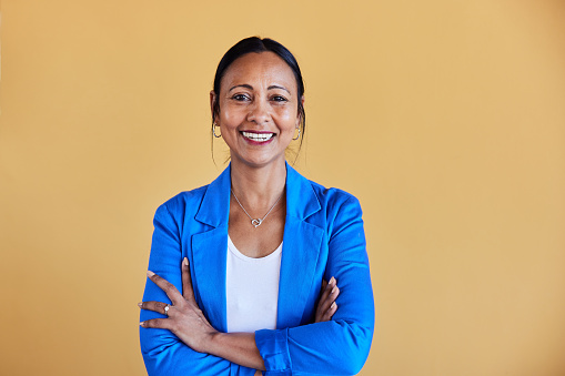 Portrait of a smiling mature businesswoman smiling while standing with her arms crossed in front of a yellow wall in an office