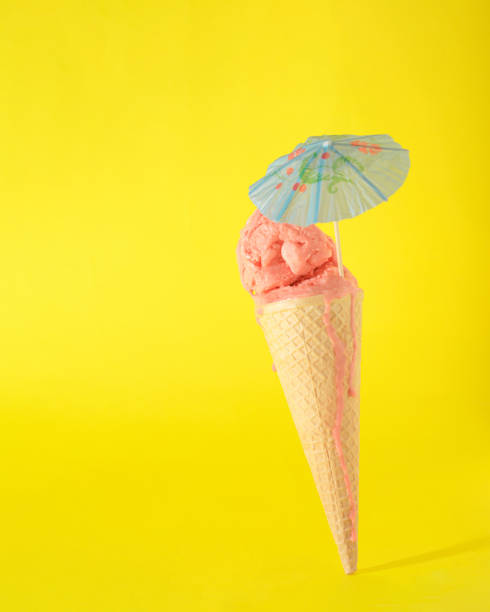 istock Ice cream cone on a vibrant yellow background with cocktail umbrella. 1411014045