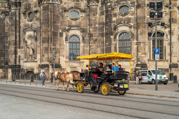Dresden, Germany - May 10, 2022: Tourists in a historic yellow carriage in front of the Hofkirche in Dresden at day.