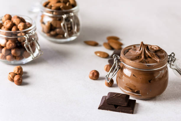 istock Hazelnut and Almond Spread with Nuts and Chocolate Bar Glass Jars with Hazelnuts Almonds and Chocolate Gray Background Horizontal Copy Space 1411015848