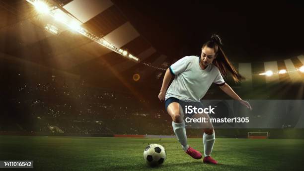 Female Soccer Football Player Dribbling Ball In Motion At Stadium During Sport Match Over Evening Sky Background Stock Photo - Download Image Now