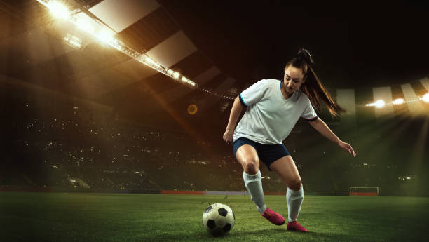 female soccer, football player dribbling ball in motion at stadium during sport match over evening sky background. - women young adult isolated length imagens e fotografias de stock