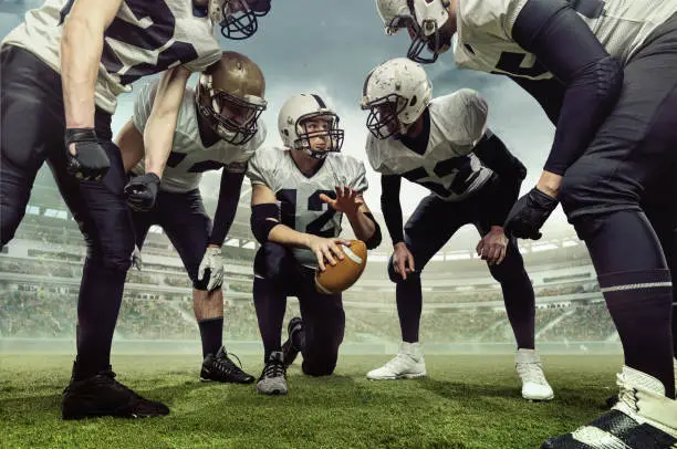 Teammates. Team of male american football players before sport match at stadium over cloudy sky background with flashlights. Concept of sport, challenges, goals, strength.