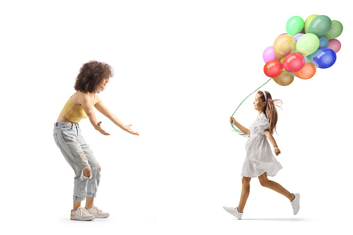 Full length profile shot of a girl with balloons running towards a young woman isolated on white background
