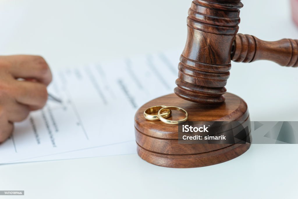 Divorce Process Weeding rings and gavel with a person signing a contract in the background. Representing justice divorce process. Arguing Stock Photo Divorce Process Weeding rings and gavel with a person signing a contract in the background. Representing justice divorce process. Arguing Stock Photo