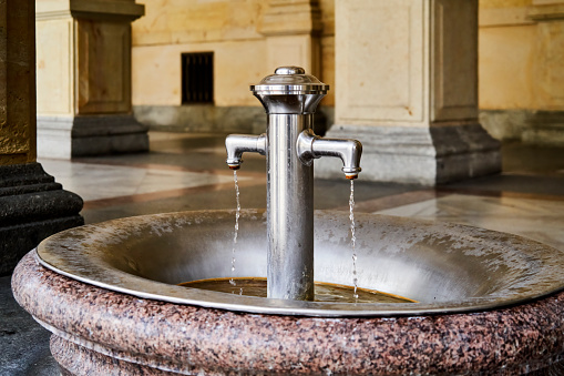 Karlsbad, Czech Republic, June 29, 2022: With granite and chromed iron set spring with medicinal water in Karlovy Vary, from which visitors and sick people can help themselves free of charge