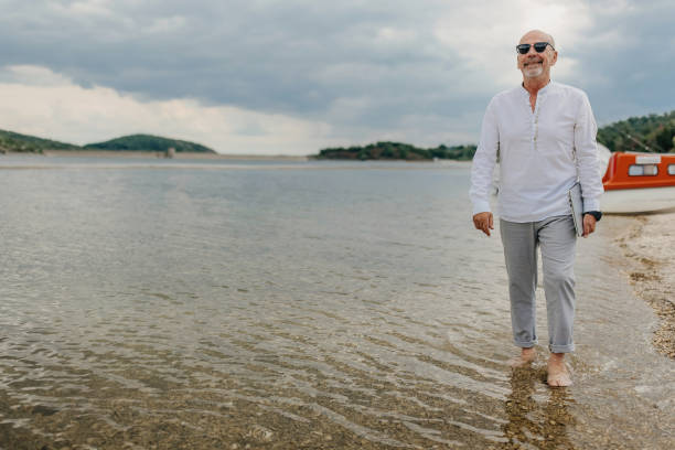 Senior man using holding laptop and walking by the beach