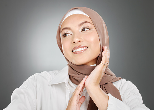 Beautiful muslim woman posing in a studio wearing a hijab. Headshot of a happy and confident arab model standing against a grey background. Fashionable woman wearing a headscarf