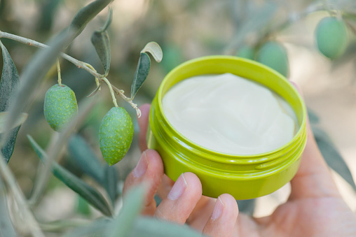 Female hand holding moisturizer in hand under olive tree branch. Representing olive fruit as  moisturizer ingredient.