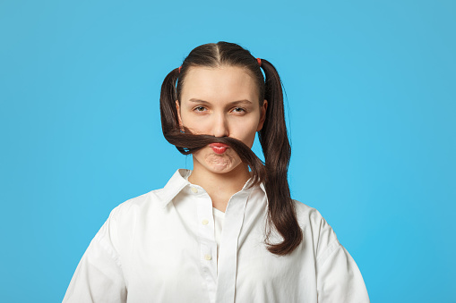pretty young woman on blue background making mustache with her hair