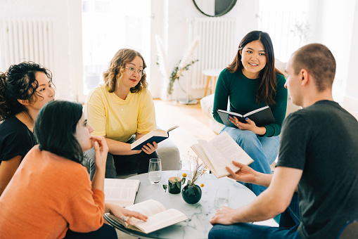 Group of multiracial people reading together at home. Book club members discussing a book at home.