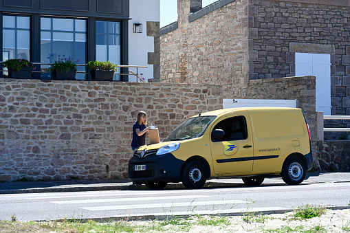 Erquy, France, 9 July, 2022 - Postal worker standing next to her post car