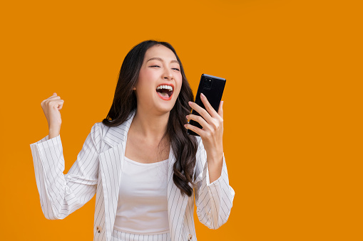 exited surprise face expression asian business woman female hand gesture exited with successful progress result on smartphone screen display  exited raised hands up isolated on bright yellow color
