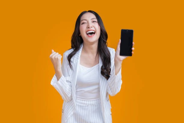 exited surprise face expression asian business woman female hand gesture exited with successful progress result on smartphone screen display  exited raised hands up isolated on bright yellow color stock photo
