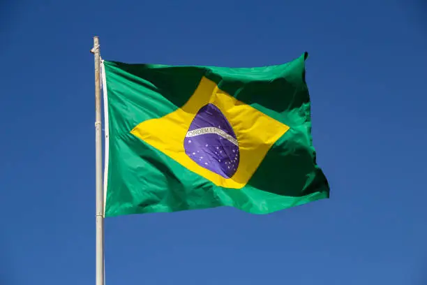 Brasília, Federal District, Brazil – July 23, 2022:  Brazilian flag flying and fluttering in the wind with blue sky in the background.
