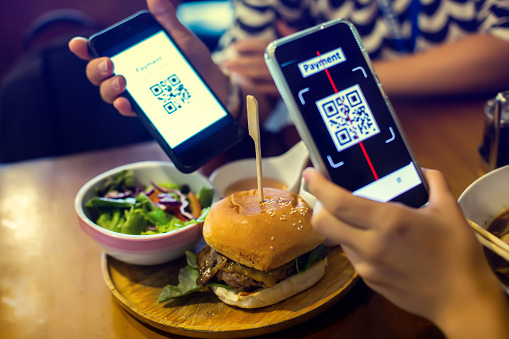 Selective focus to hamburger with blurry Smartphone in hand to scan QR code payment tag in restaurant to accepted generate digital pay without money. Qr code payment concept.