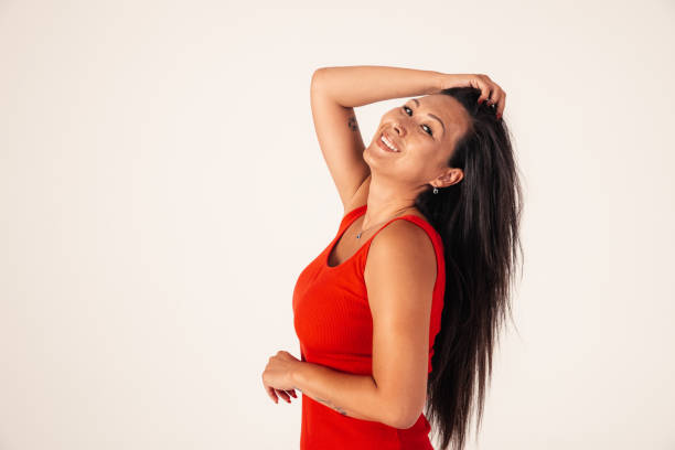 West Asian model going for portrait photos in studio. In this photo, she is standing and smiling with her head up and her hand touching her hair, looking at camera.