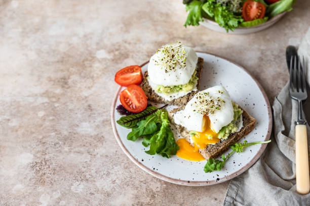 istock Sourdough bread with cream cheese, mashed avocado and poached egg served with salad, tomatoes and sprouts on concrete background. Healthy breakfast or brunch. Diet food concept. 1411026296