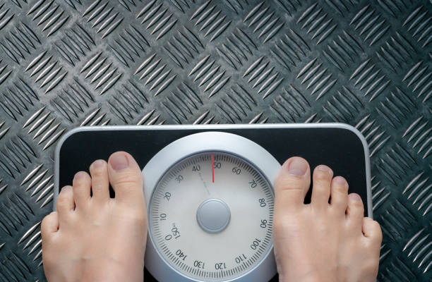 Top view of feet on weighing scale. Women weigh on a weight balance scale after diet control. Healthy body weight. Weight and fat loss concept. Weight measure machine. Body Mass Index or BMI concept. vista superior de los pies en báscula de pesaje. las mujeres pesan en una báscula de equilibrio de peso después del control de la dieta. peso corporal saludable. concepto de pérdida de peso y grasa. máquina de medición de peso. Índice de masa corpor