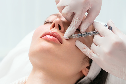 Lip augmentation and correction procedure in a cosmetology salon. The specialist makes an injection in the patient lips