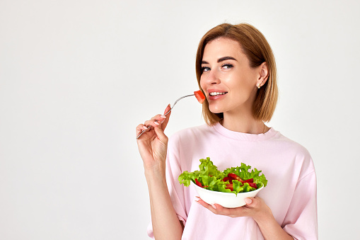 beautiful smiling healthy woman eating fresh vegetable salad, looking happy on white background. copy space