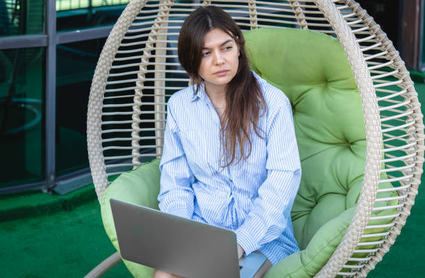 istock Serious young woman works on a laptop while sitting in a hammock. 1411034546