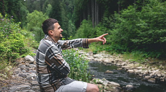 A young man in a plaid shirt in the forest by the river enjoys nature, wildlife.