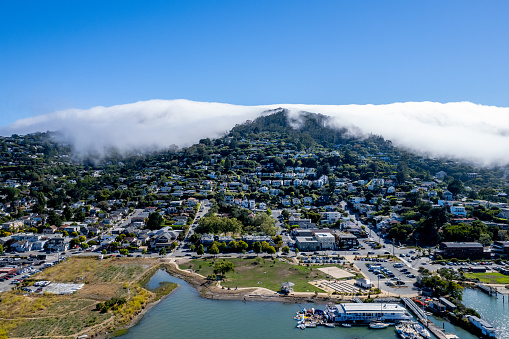 Aerial view of Sausalito on a sunny day with fog pouring over the hillside. View of Bay and marina.