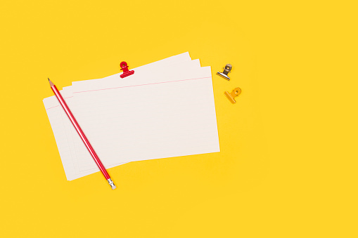 Blank striped paper notes with a red pencil on a yellow background with copy space