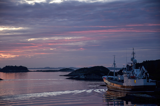 Beautiful colorful pink sunset over a Norwegian sea and archipelago by summer with a big boat in the harbor