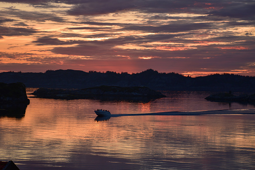 Beautiful colorful sunset over a Norwegian sea by summer with a fisherman boat gliding on the water
