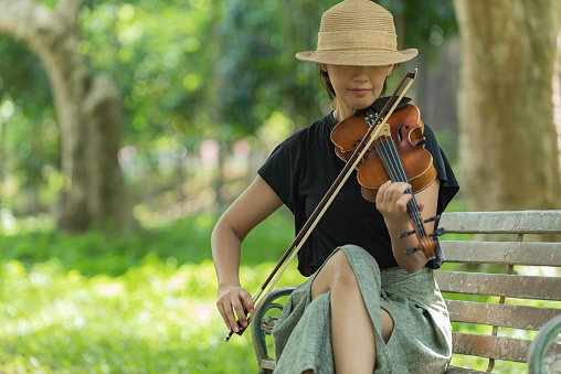 Beautiful asian woman hold violin on nature background, in emotion happy feeling.