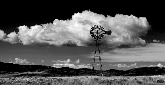 Windmill on hillside in countryside rural America with sky and clouds black and white