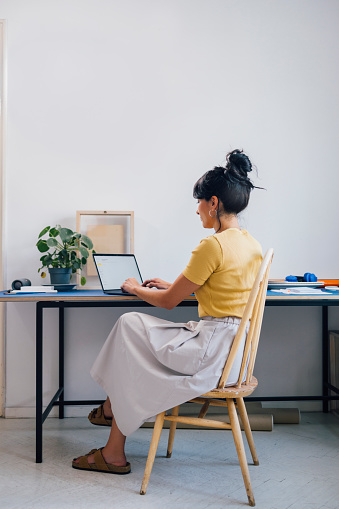 A back view of a pensive casually dressed businesswoman typing on her computer.