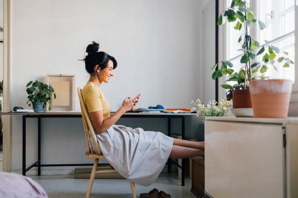 A Smiling Caucasian Female Businesswoman Texting On Her Mobile Phone While Sitting At Home A side view of a happy beautiful influencer reading updates on social networks using her smartphone while relaxing. happy using phone stock pictures, royalty-free photos & images