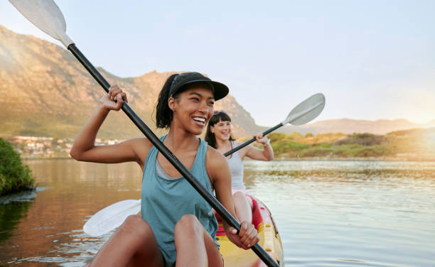 deux amis souriants faisant du kayak sur un lac ensemble pendant les vacances d’été. des femmes souriantes et joyeuses et enjouées se lient à l’extérieur dans la nature avec l’activité de l’eau. s’amuser sur un kayak pendant les loisirs de  - kayaking photos et images de collection