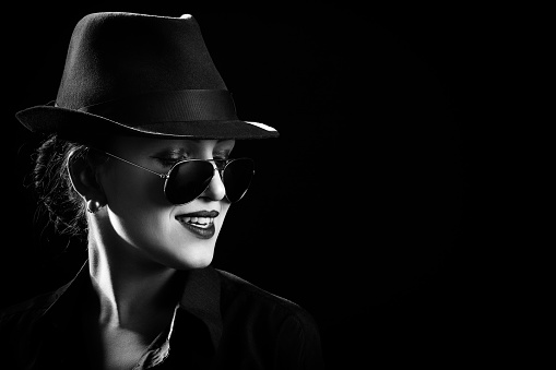 woman with hat and sunglasses on black background with copy space, smiling, monochrome