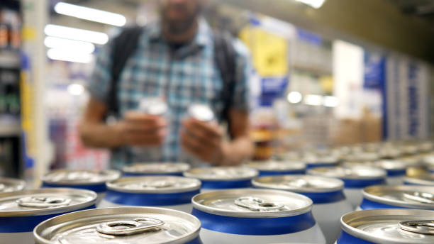 Close-up of many aluminium cans of beer or another drink on a store shelf and a male buyer takes a couple stock photo