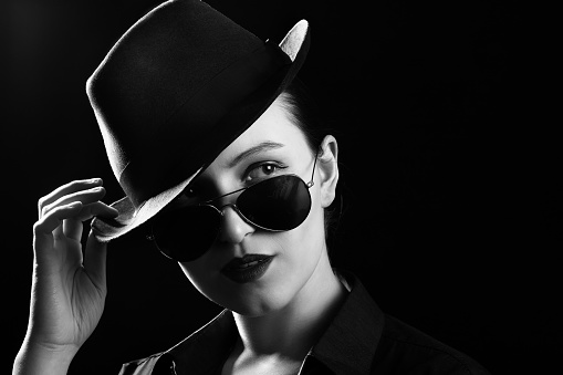 woman with hat and sunglasses on black background with copy space, monochrome