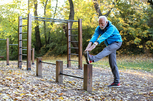 Senior man stretching in an autumn park. About 65 years old, Caucasian male.