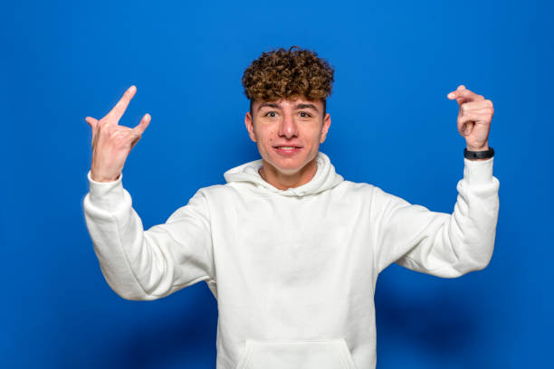 istock A handsome young man with curly hair isolated over blue background screaming with a crazy expression making a rock symbol with his hands up. Music star heavy concept. 1411053792