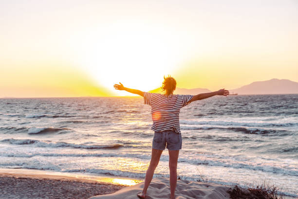 Woman standing on the beach with her arms wide open while enjoying the sunset.