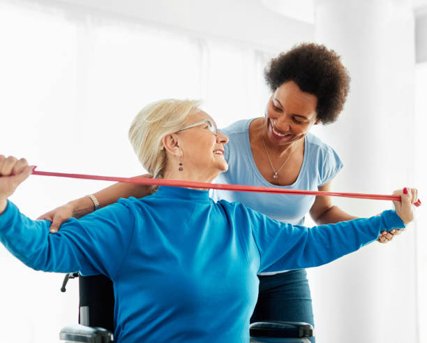 senior care exercise physical therapy exercising help assistence retirement home physiotherapy physiotherapist fitness gym strech band clinic therapist elderly woman band stretching - patient retirement senior adult hospital imagens e fotografias de stock