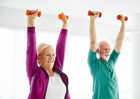 Senior couple exercise stretching and exercising with dumbbell lifting weight at home health care
