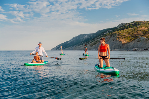 July 11, 2022. Dalaman, Turkey. Small group of active people on stand up paddle board at quiet sea. Water sport on Red Paddle SUP board in ocean.